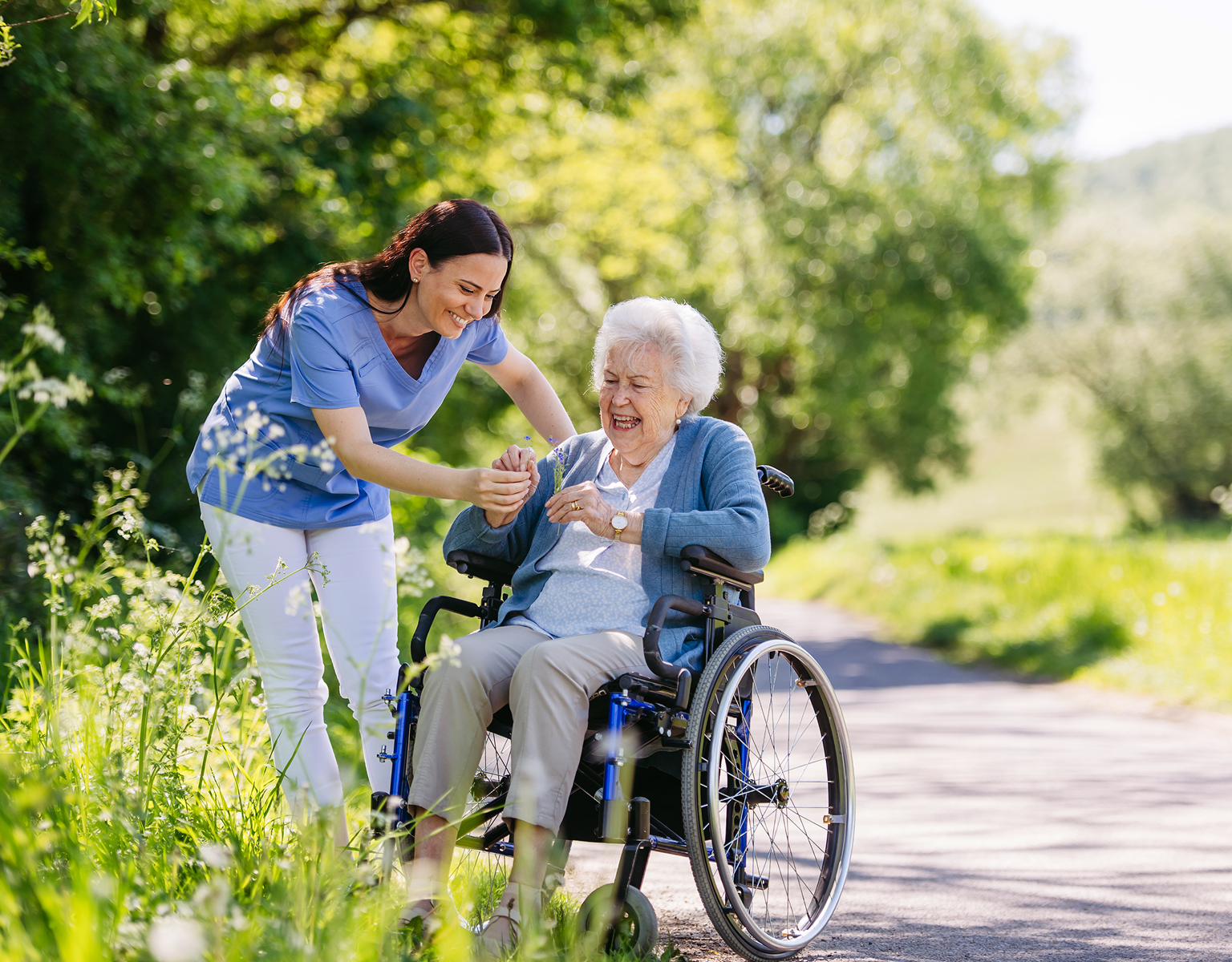 Caregiver assisting elderly woman in wheelchair outdoors.