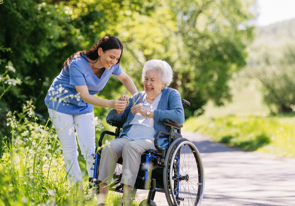 Caregiver assisting elderly woman in wheelchair outdoors.